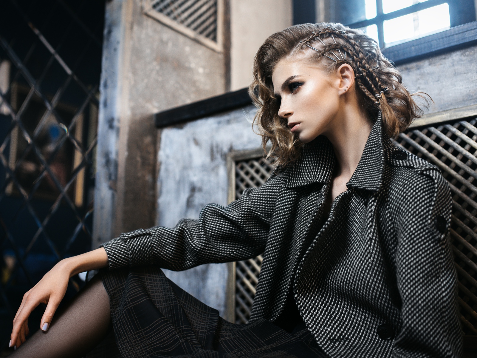 Молодая девушка в сером пальто сидит у стены