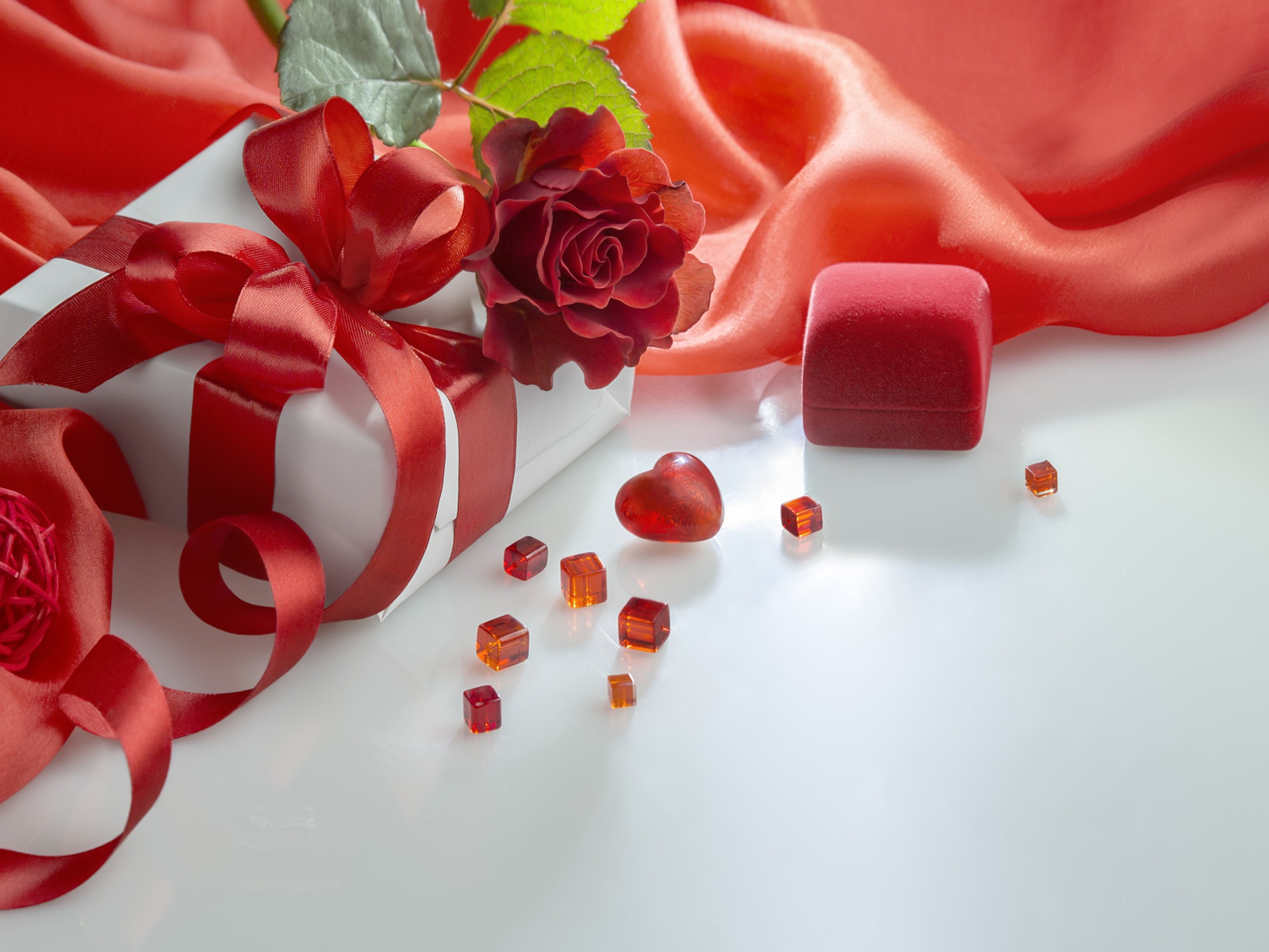Подарки на белом столе с розой и красной тканью