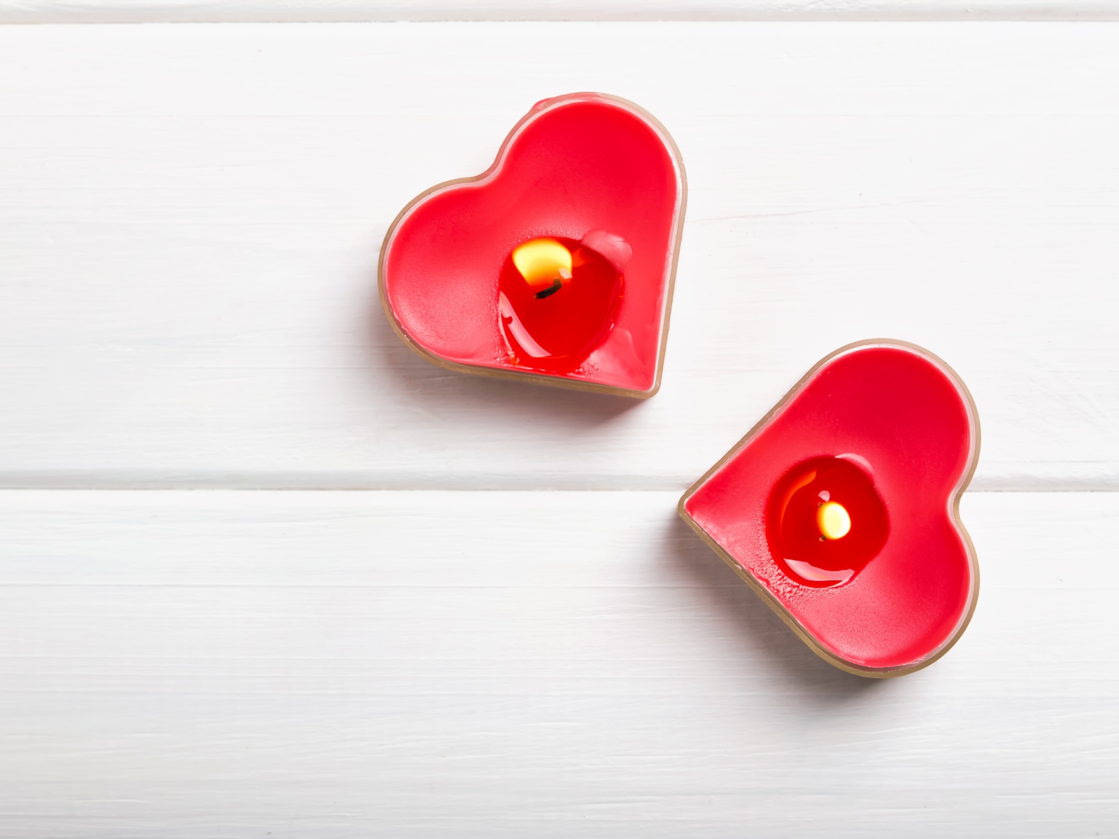 Две зажженные свечи в форме сердца на столе 
