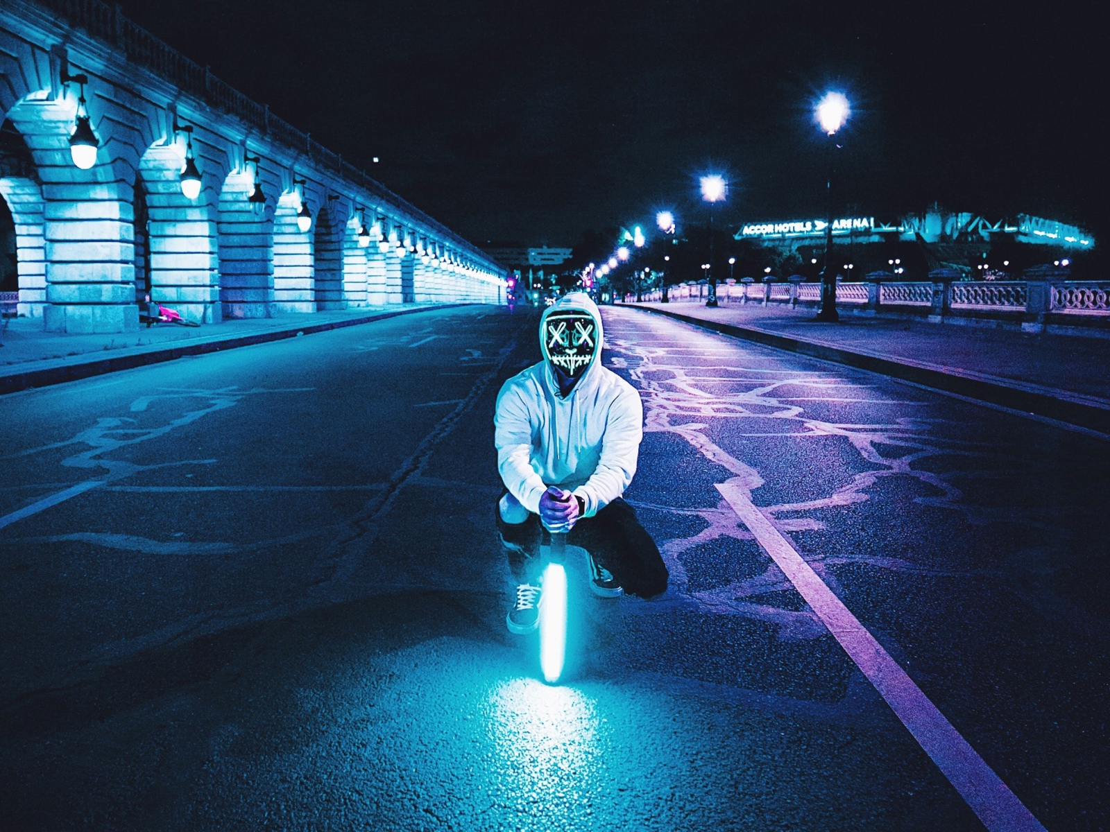 Парень в светящейся маске сидит с неоновой лампой на дороге