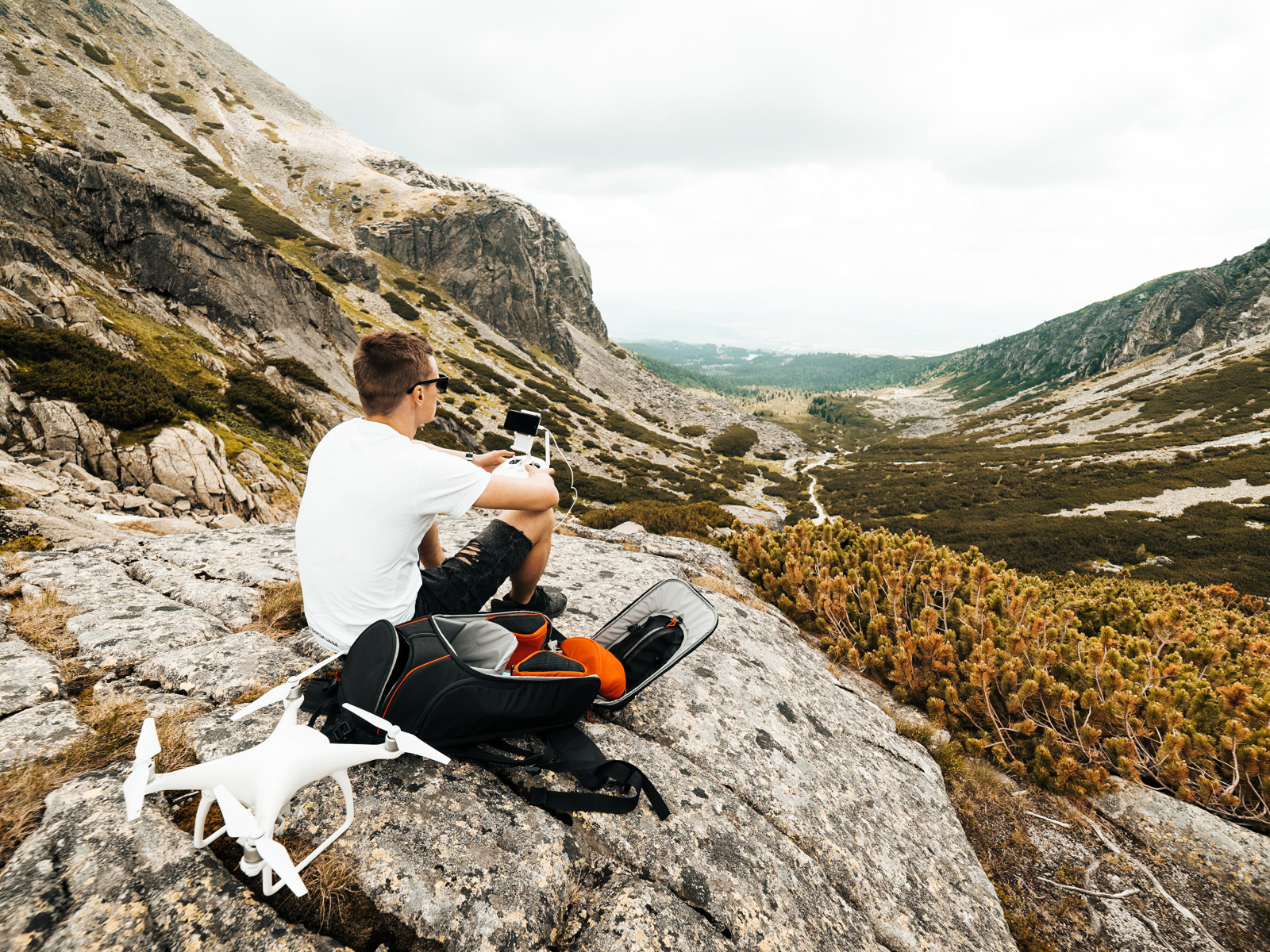Парень с квадрокоптером сидит на камне в горах 