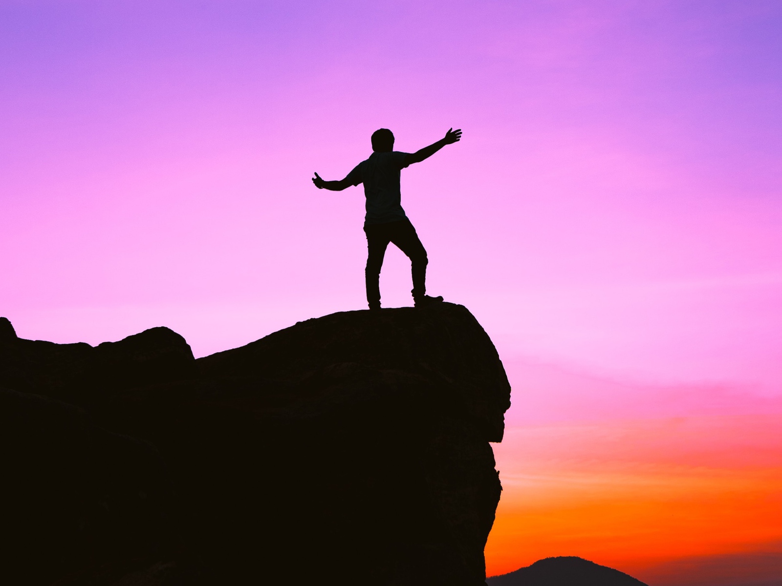 Мужчина стоит на краю утеса на закате