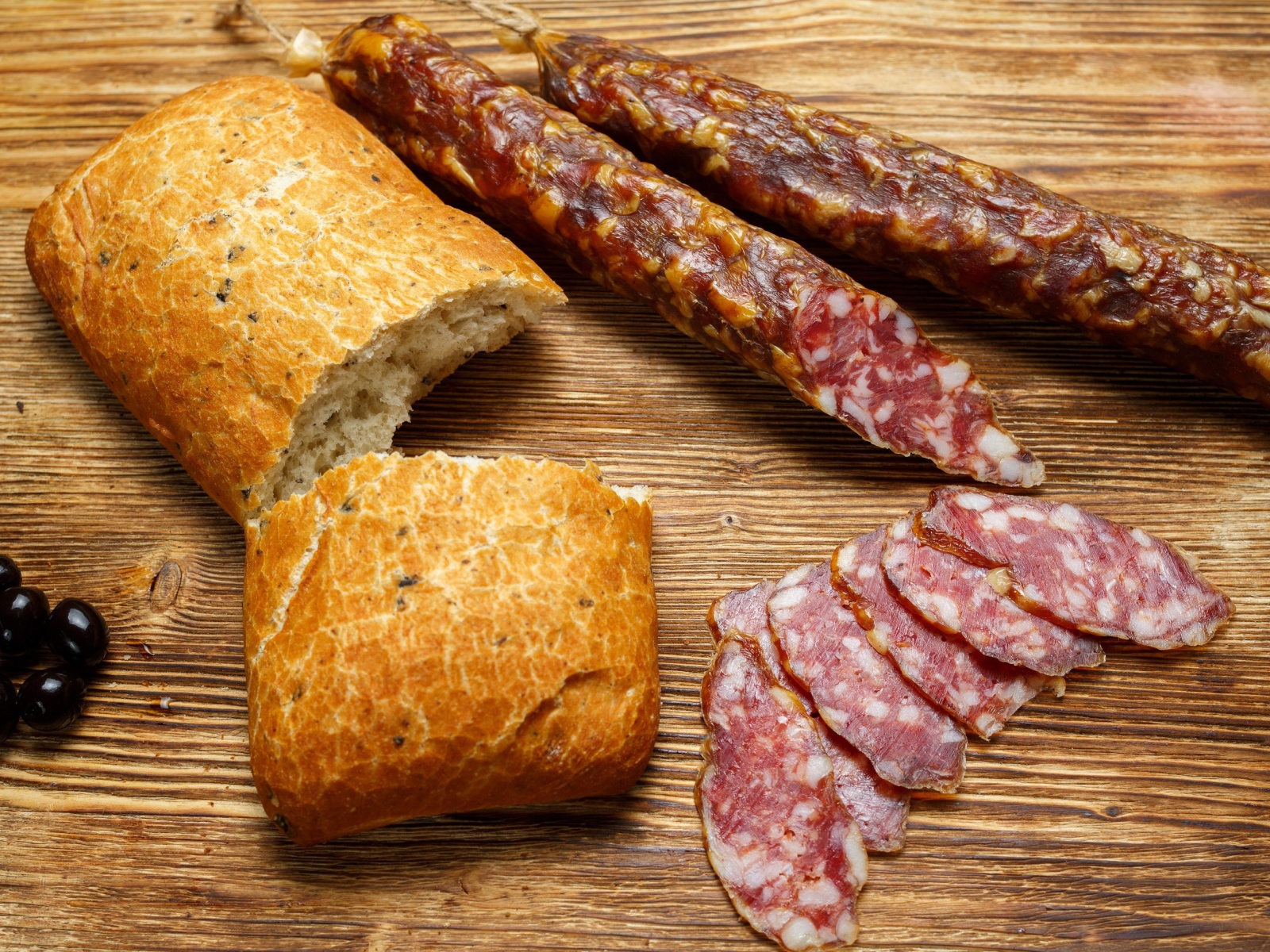 Сухая колбаса на столе с батоном и оливками