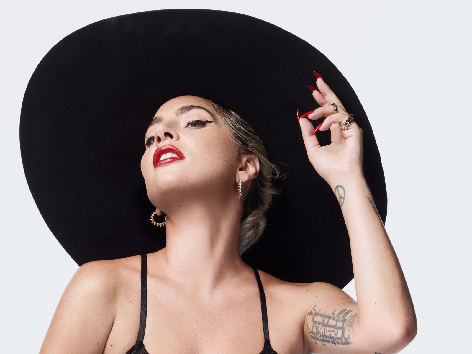 Певица Леди Гага в большой черной шляпе на белом фоне