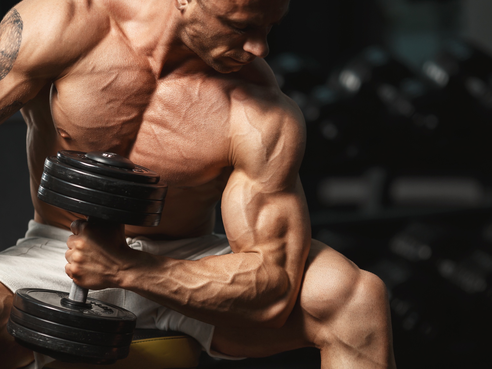 Сильный мужчина качает мускулы гантелей 