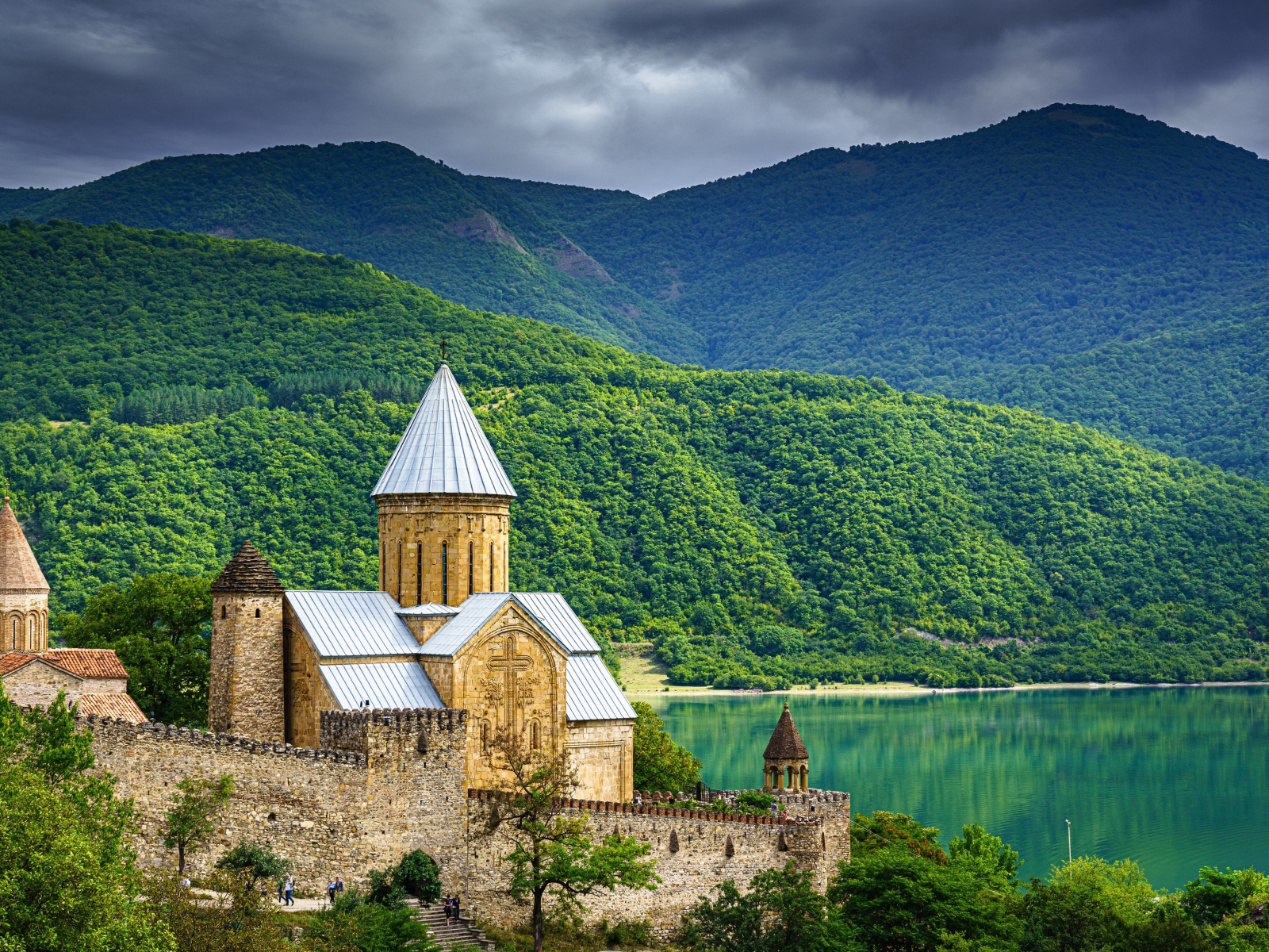 Старинный храм на берегу озера на фоне покрытых деревьями гор 