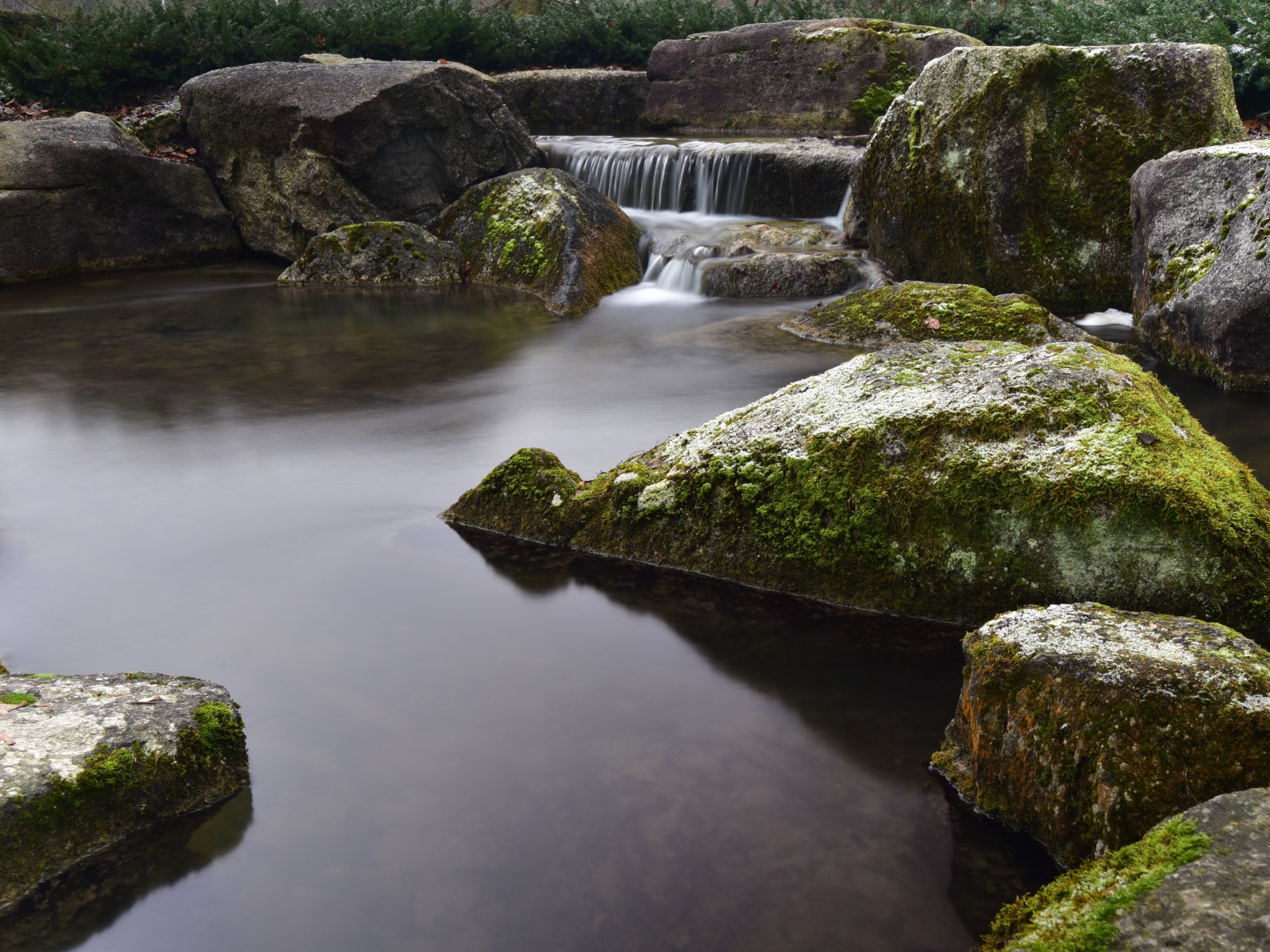 Вода стекает по камням в пруд с большими покрытыми мхом камнями