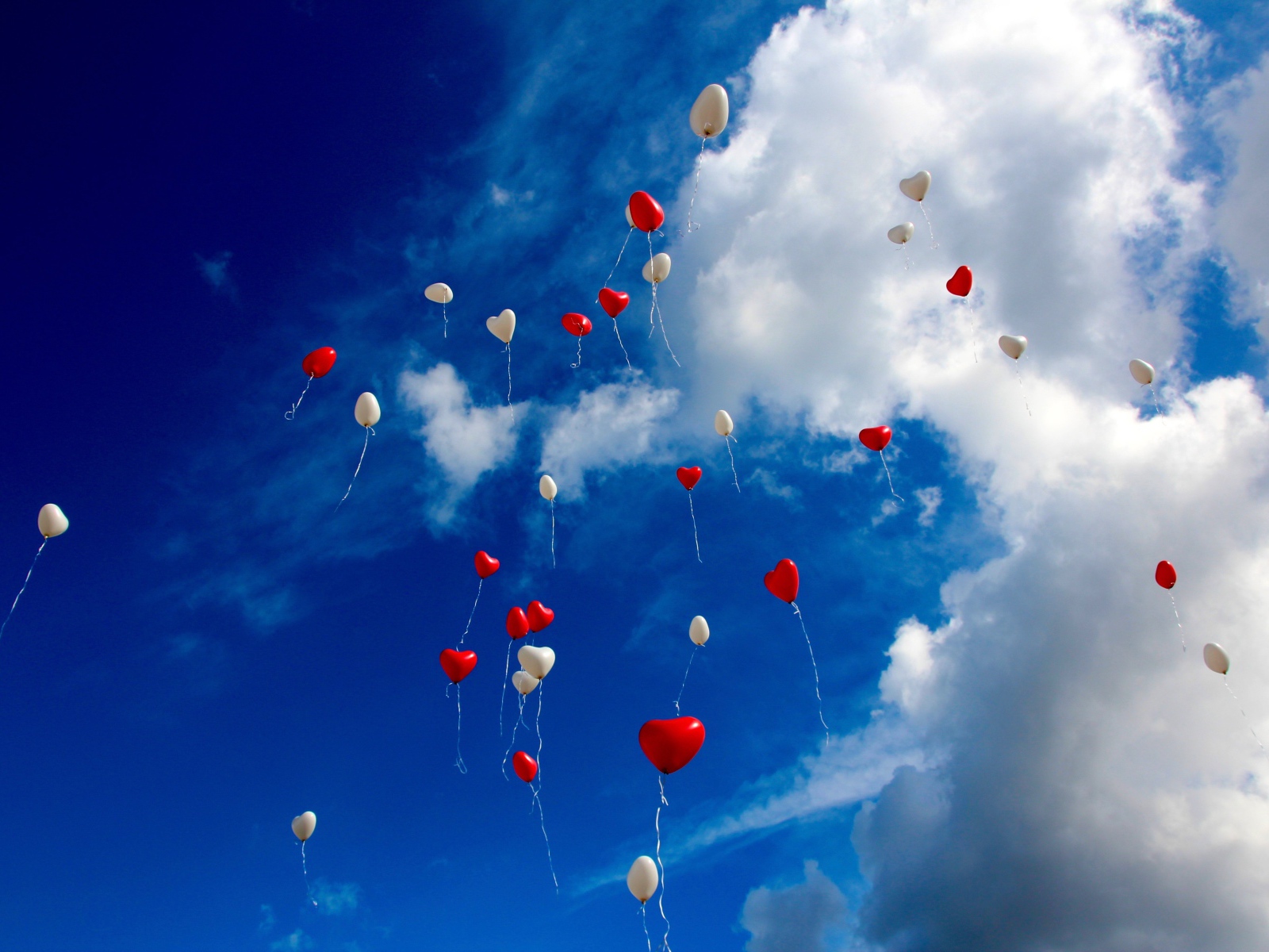 Много шариков в форме сердца в небе с белыми облаками