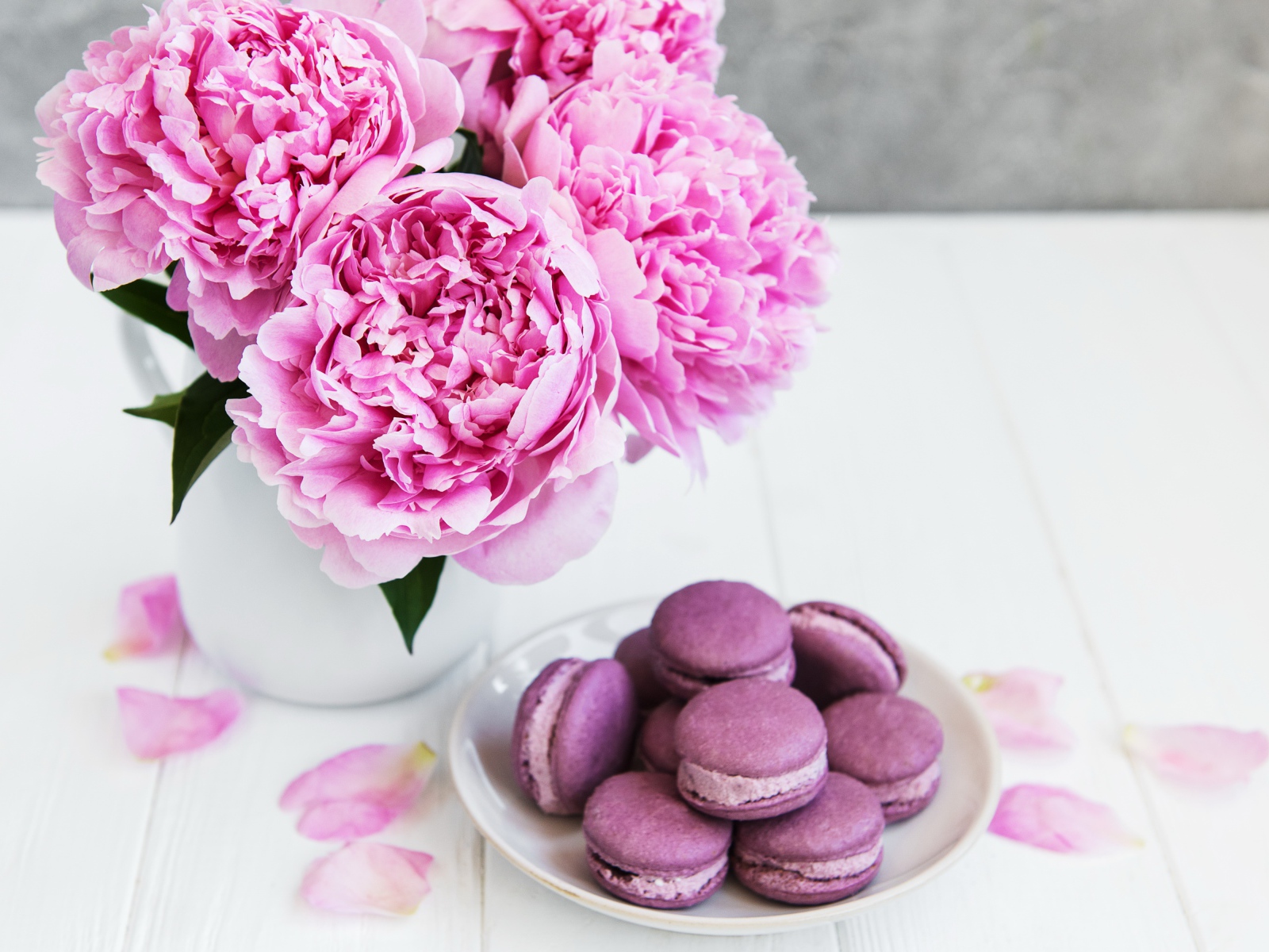 Букет розовых пионов на белом столе с десертом макарон 