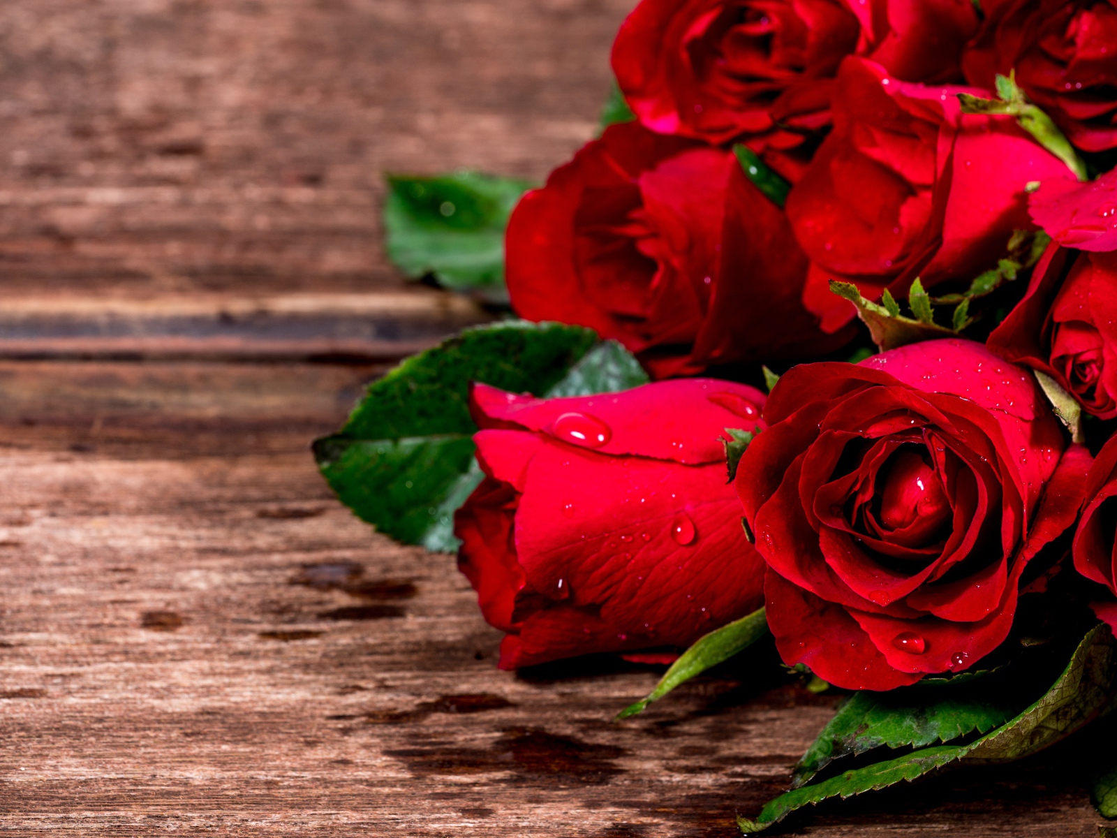 Букет красных роз на деревянном столе в каплях воды