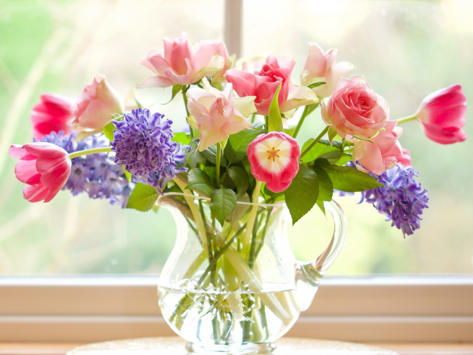 Букет роз, тюльпанов и гиацинтов в стеклянной вазе у окна