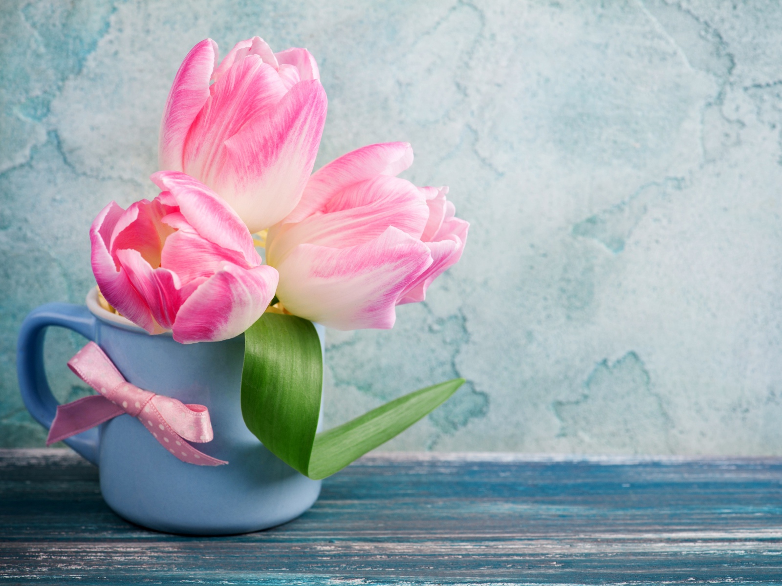 Три розовых тюльпана в чашке на столе 