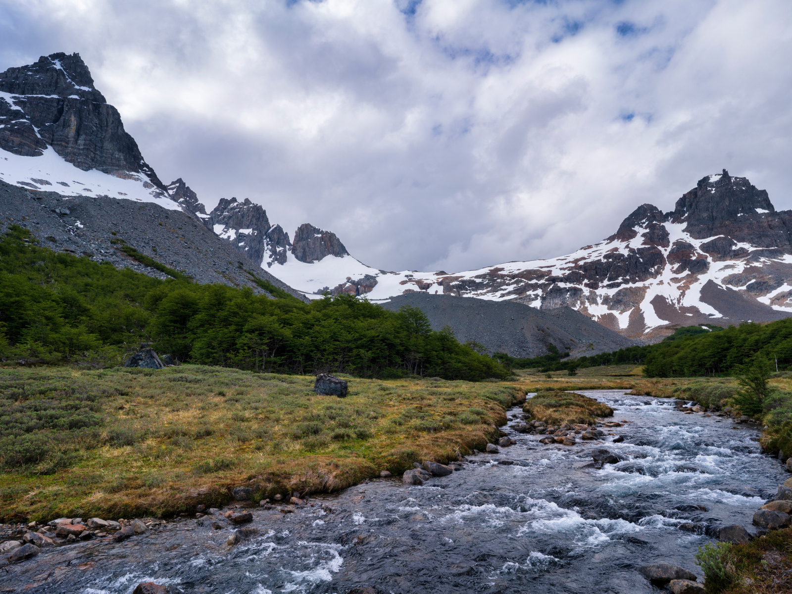 Быстрая река у заснеженных гор под густыми белыми облаками