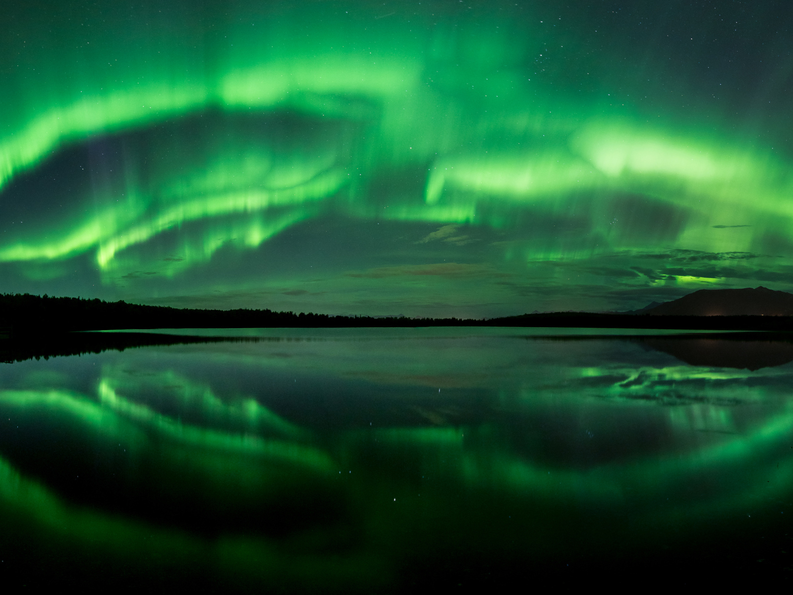 Зеленое северное сияние отражается в воде озера ночью 