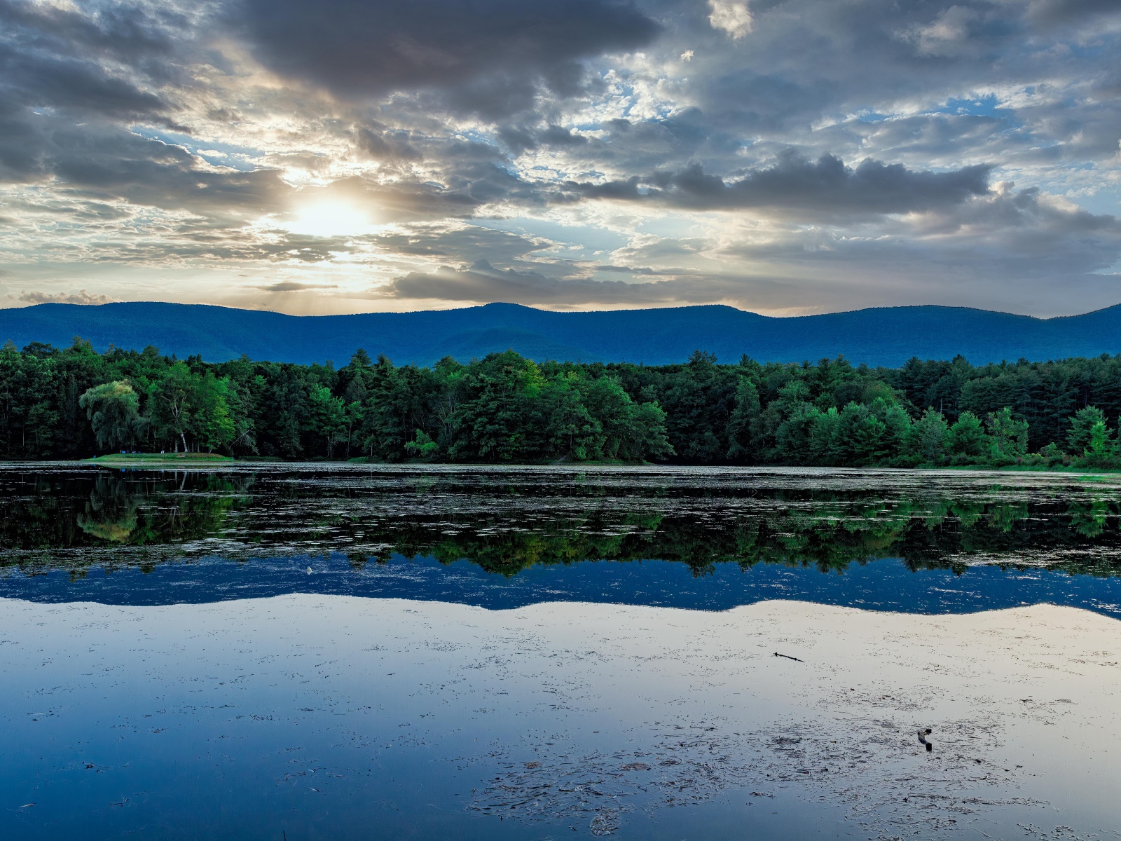 Солнце пробивается сквозь облака в небе над озером