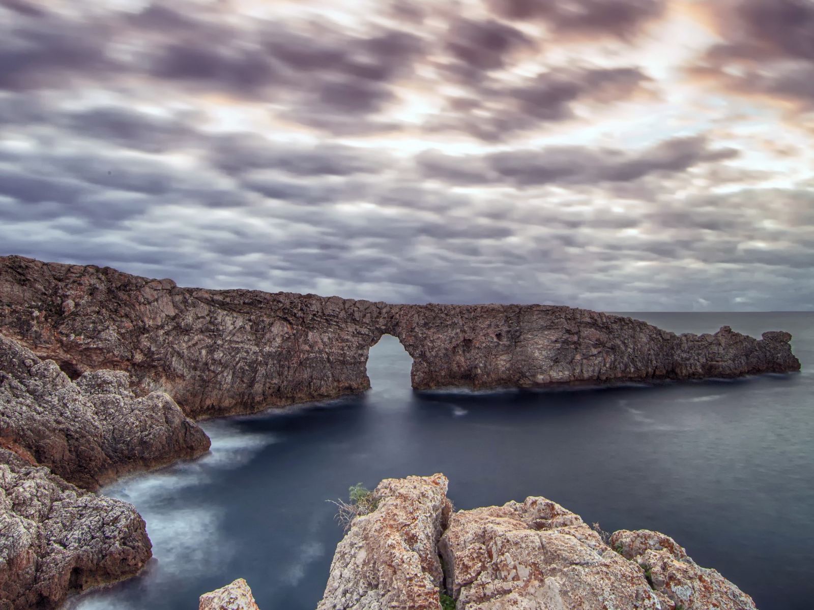Arch in the rock in the sea under a cloudy sky