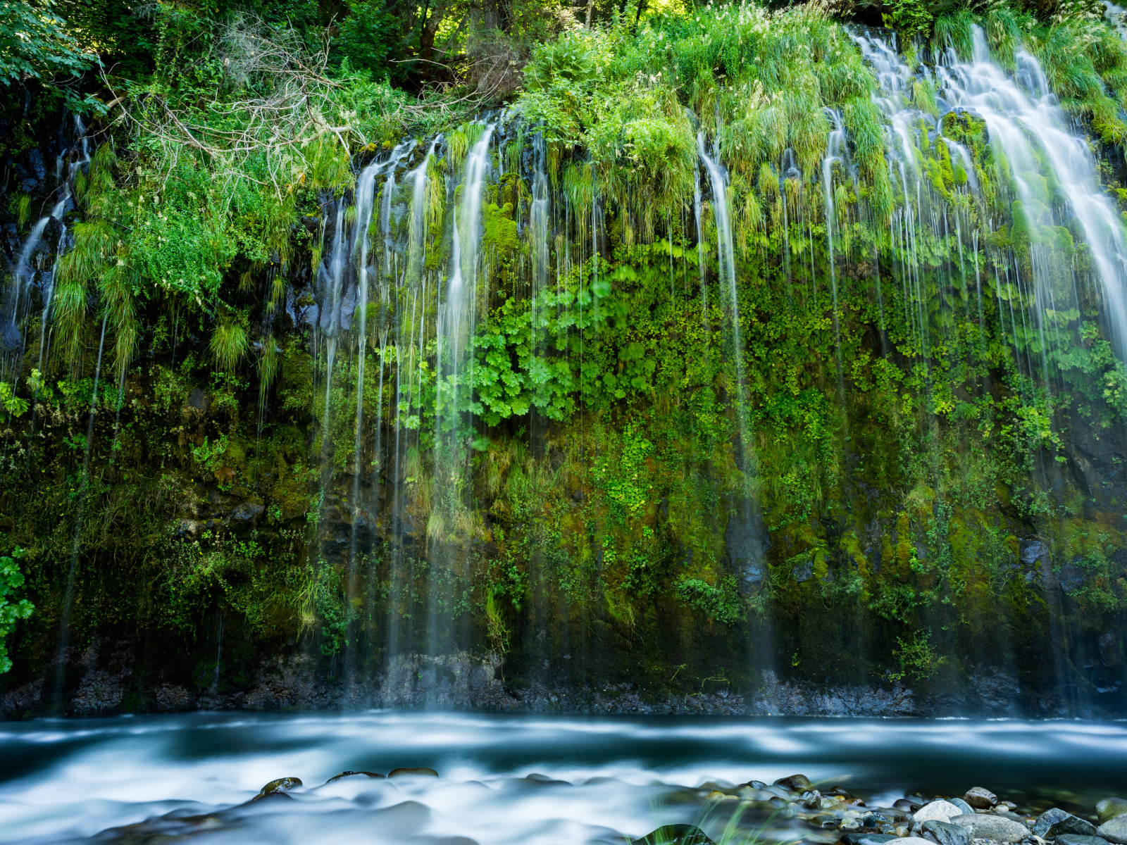 Красивый водопад стекает по покрытом зеленью утесе 