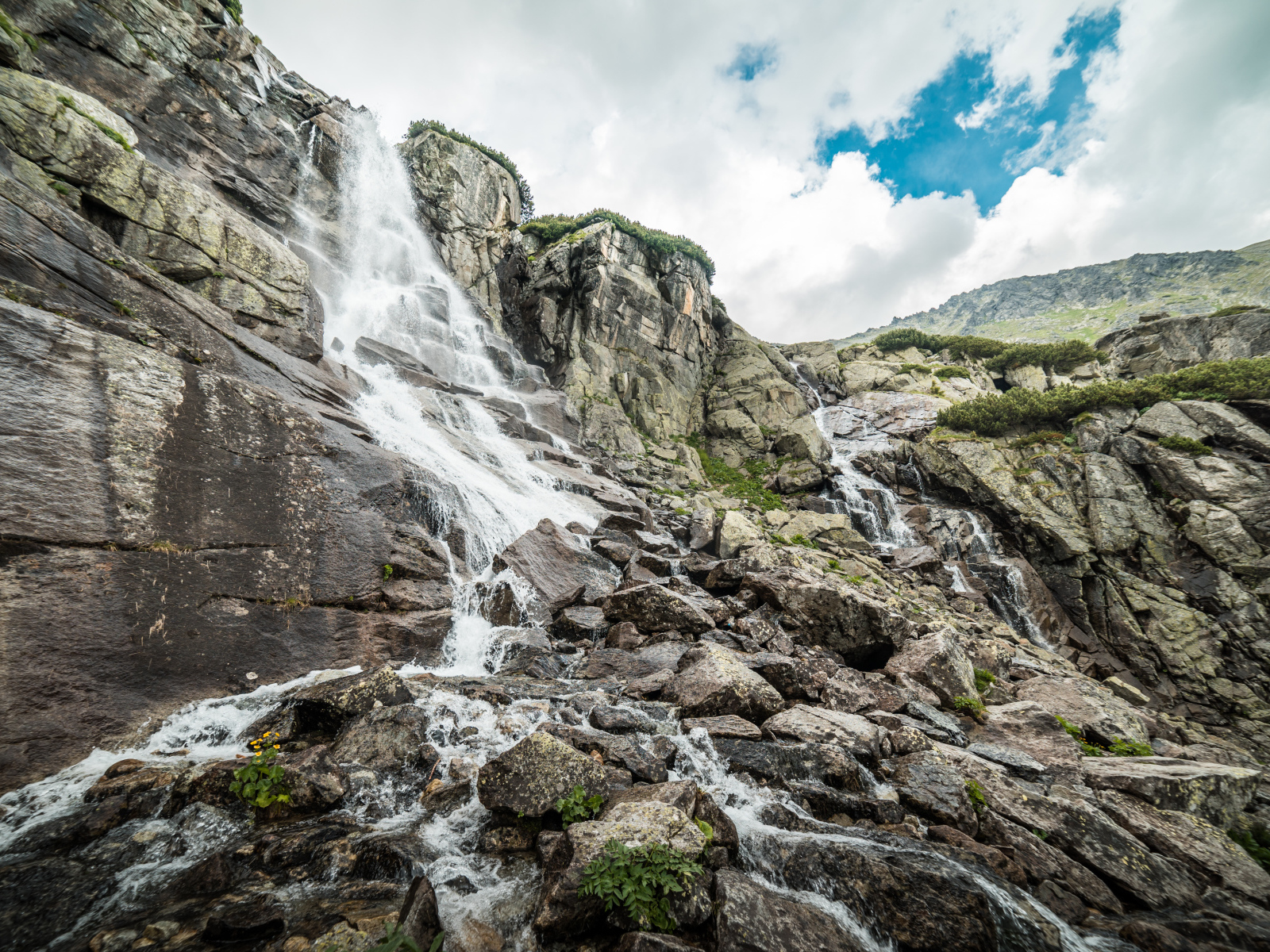 Водопад стекает по камням на фоне неба с белыми облаками