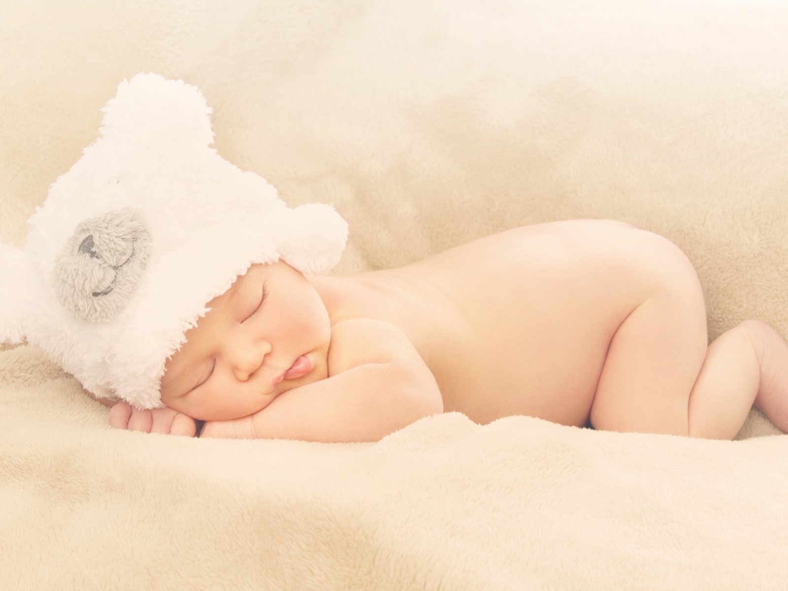 Грудной ребенок с белой шапке спит на кровати