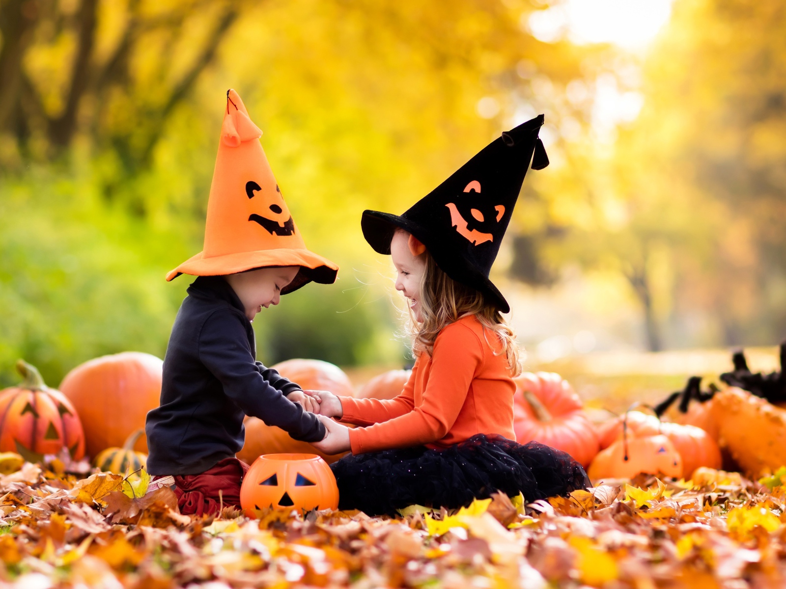 Маленькие мальчик и девочка в костюмах на Хэллоуин сидят на листве