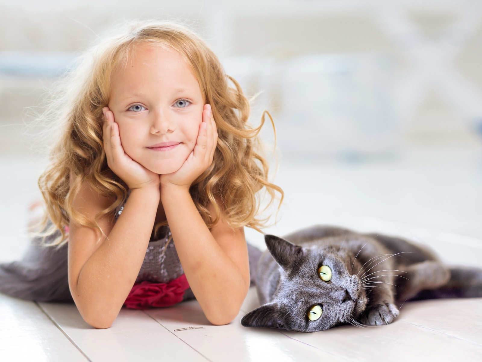 Маленькая милая голубоглазая девочка лежит на полу с котом