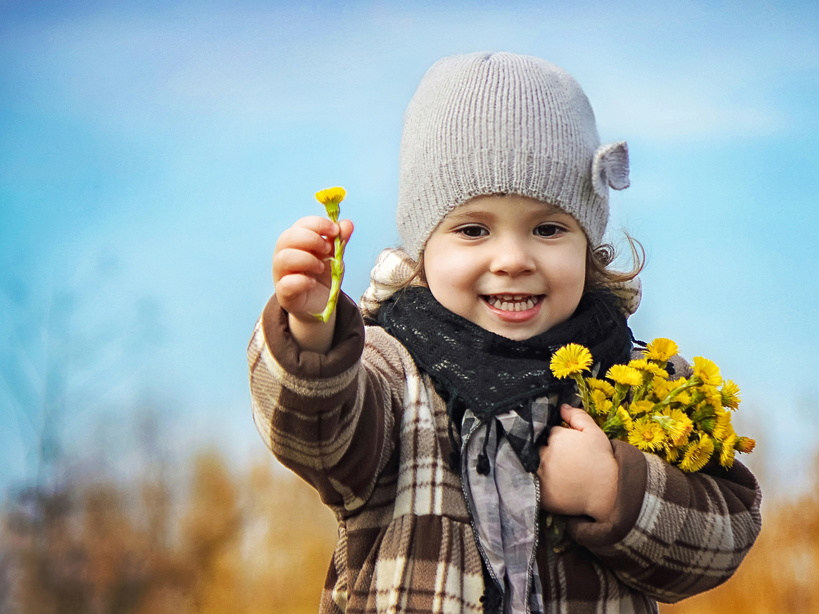 Маленькая девочка в шапке с желтыми цветами в руке
