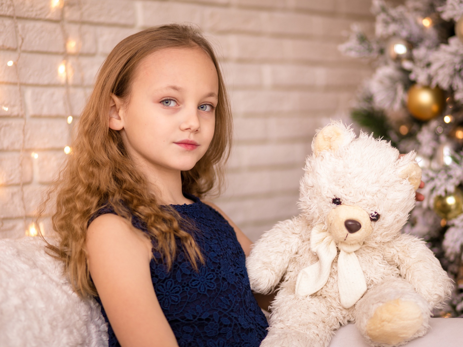 Маленькая девочка с мишкой сидит у наряженной ели 