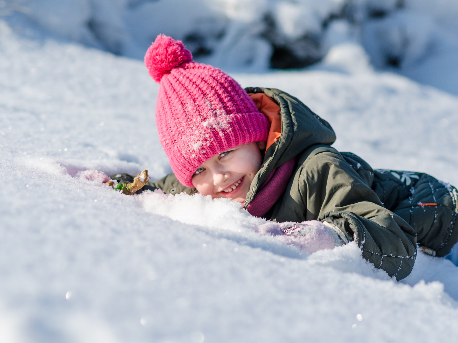 Маленькая улыбающаяся девочка лежит на снегу