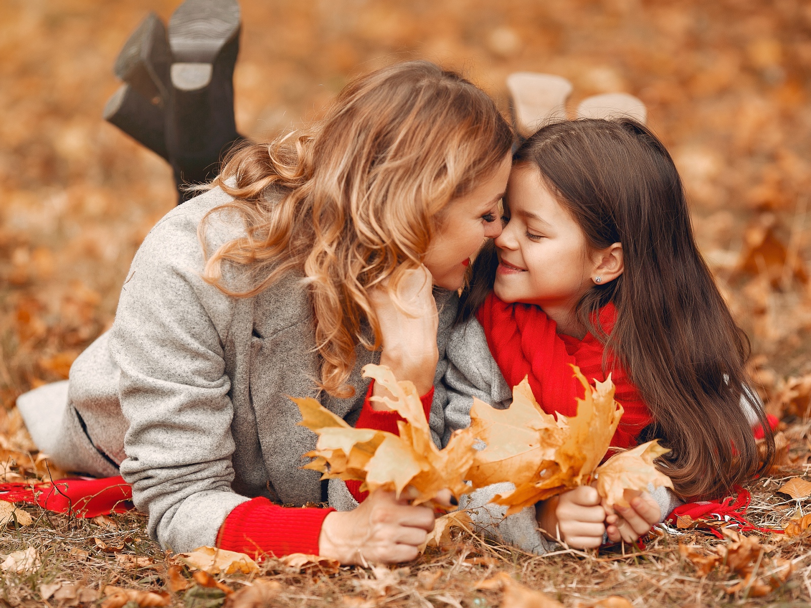 Мама с дочкой лежат на листве осенью 