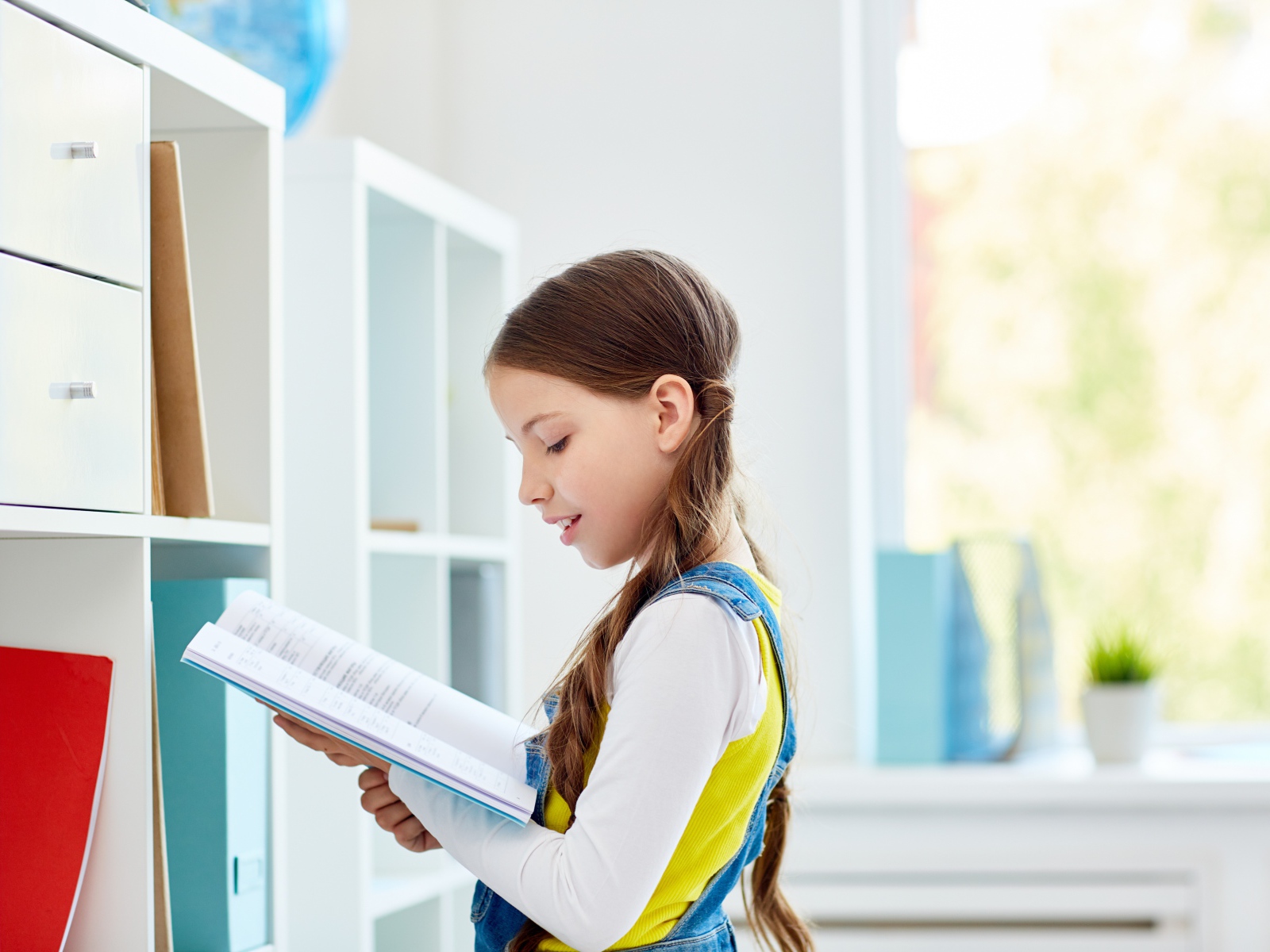 Умная девочка школьница с книгой в библиотеке 