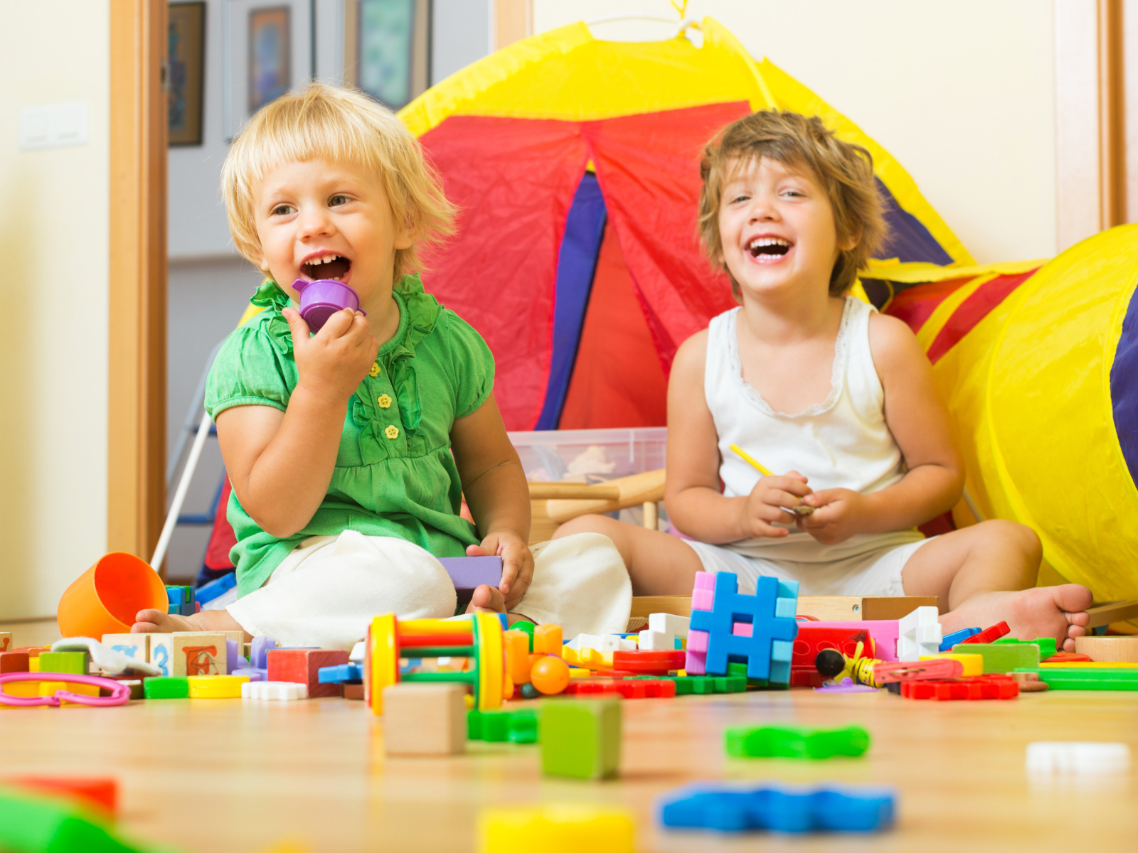 Два улыбающихся ребенка играют с конструктором 