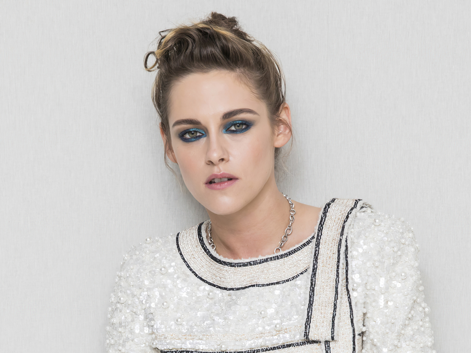 Актриса Кристен Стюарт с накрашенными глазами на фоне серой стены 