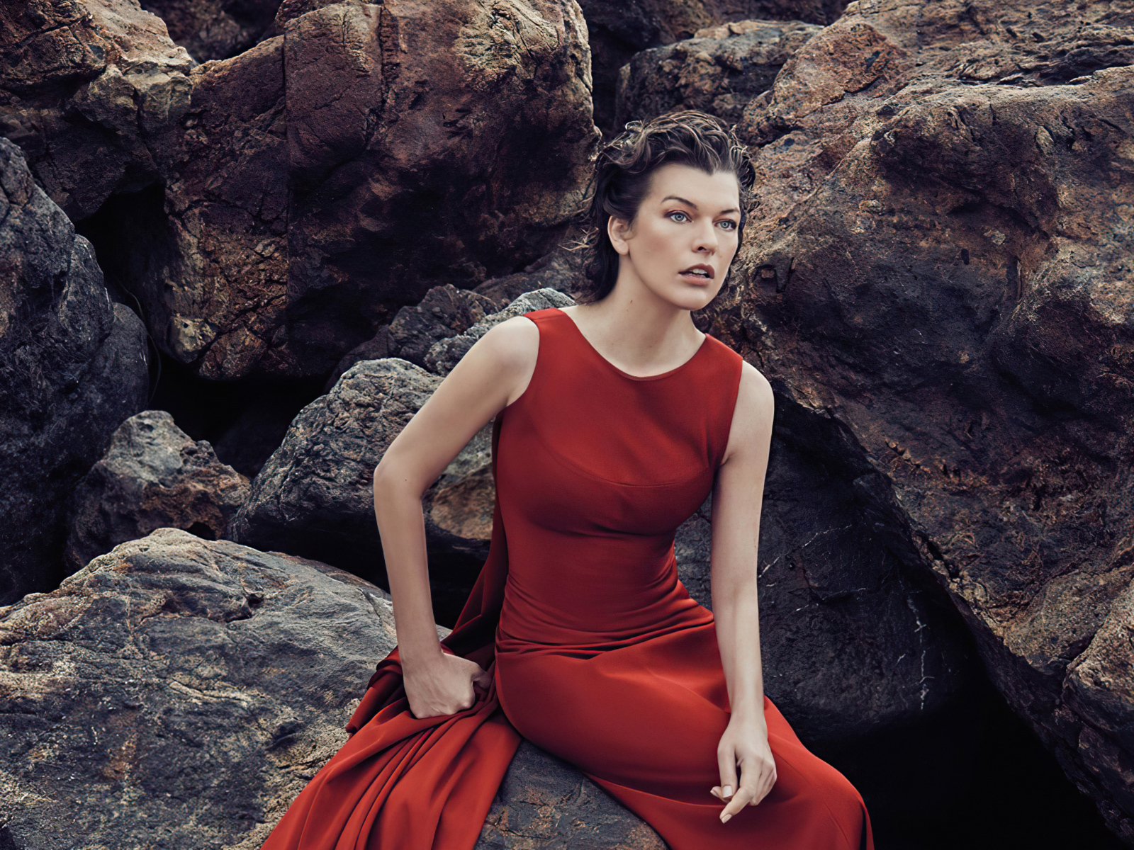 Актриса Милла Йовович в красном платье сидит на камне