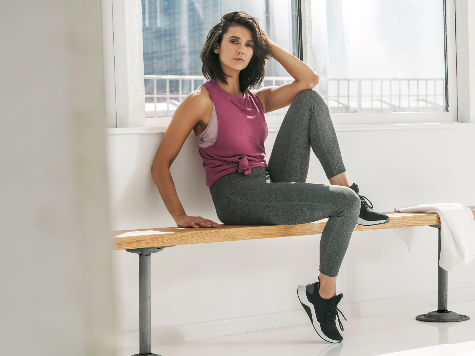 Актриса Нина Добрев сидит на лавке в спортивном костюме