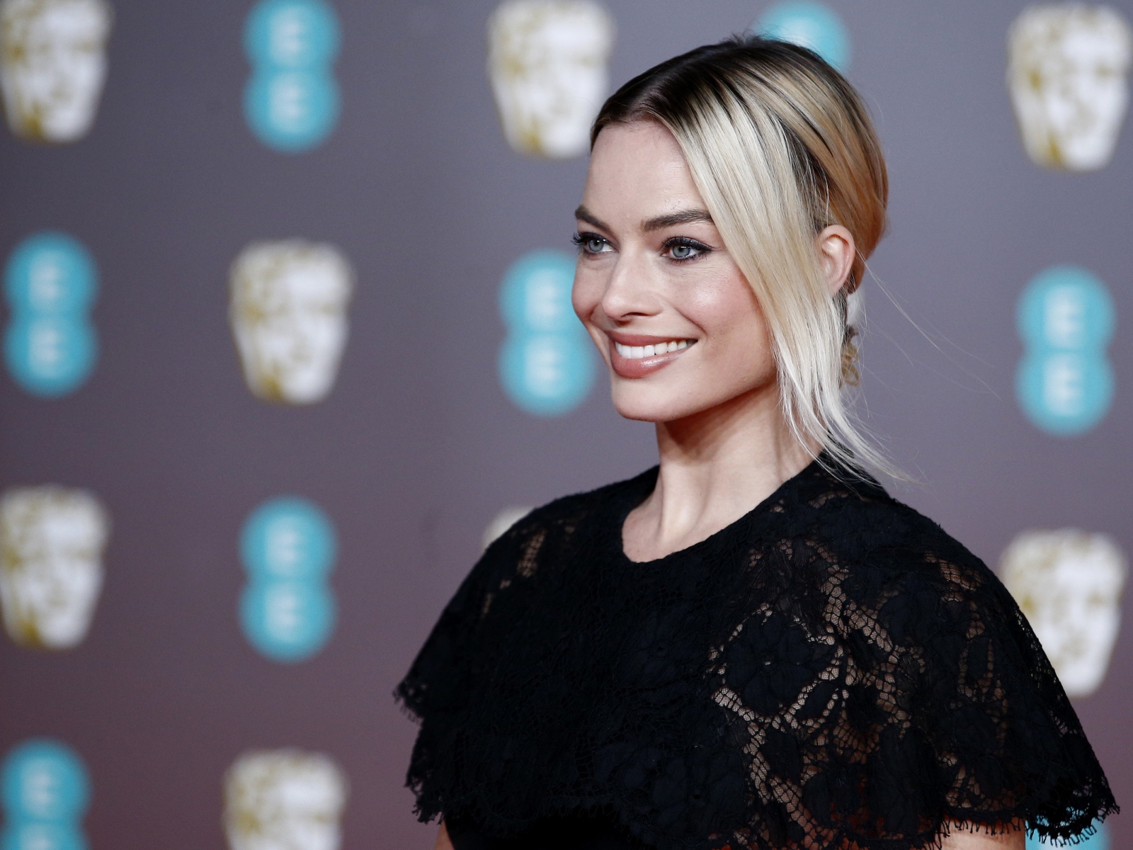 Улыбающаяся актриса Марго Робби в черном платье 