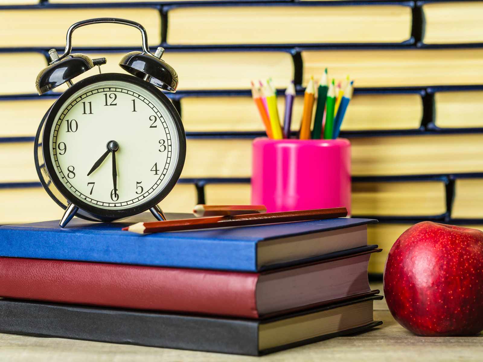 Будильник, книги, карандаши и яблоко на столе у стены 
