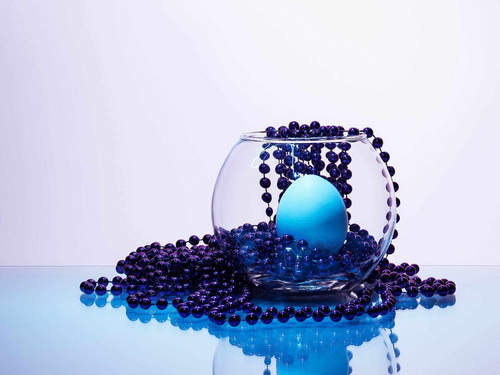 Синие бусы на столе со стеклянной вазой и яйцом