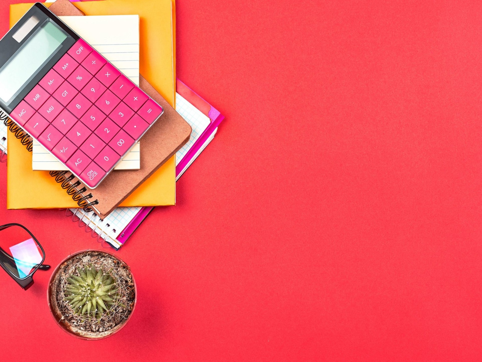 Калькулятор с очками и блокнотами на розовом фоне 