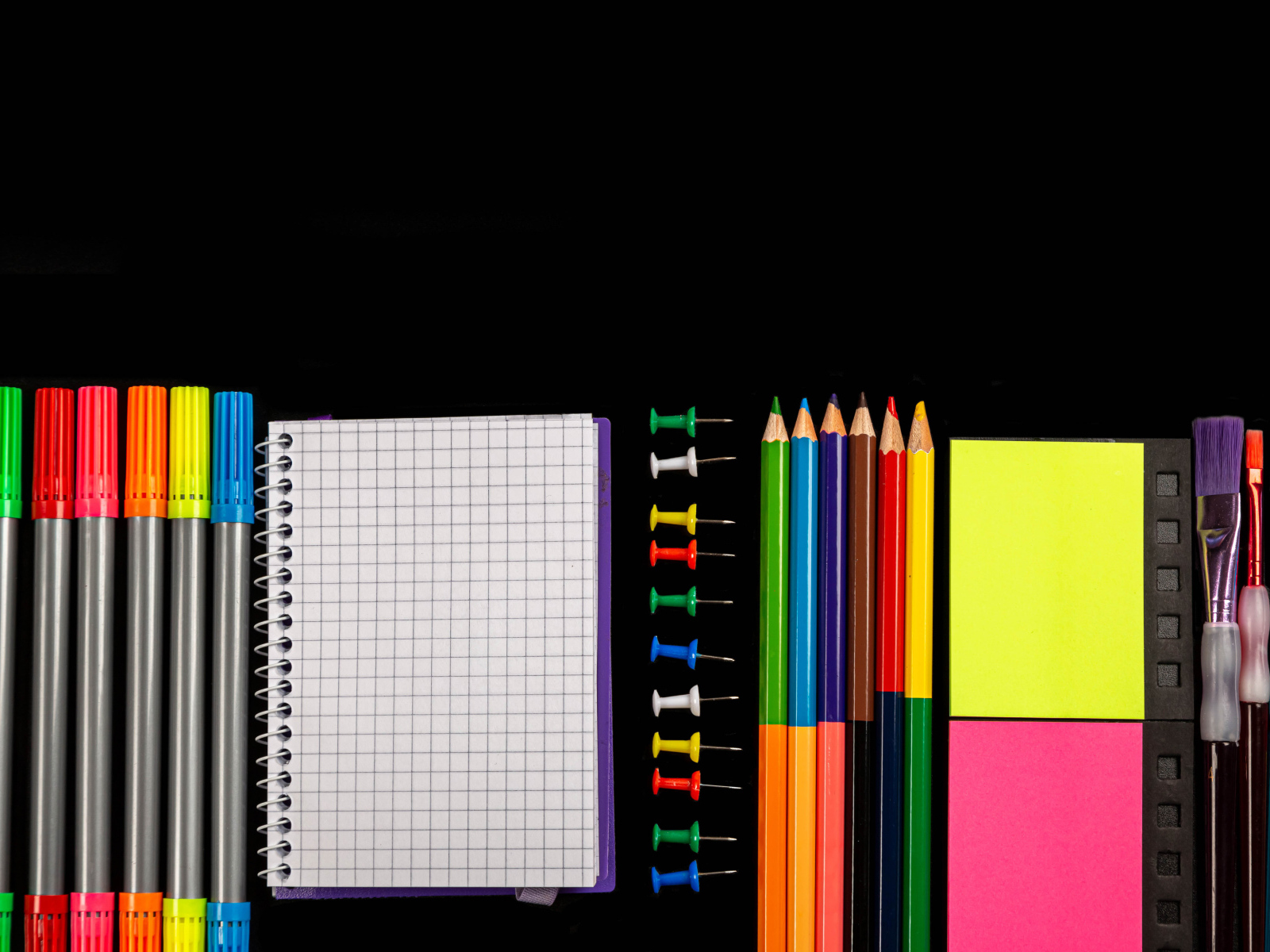 Felt pens, pencils, notebook and brushes on black background