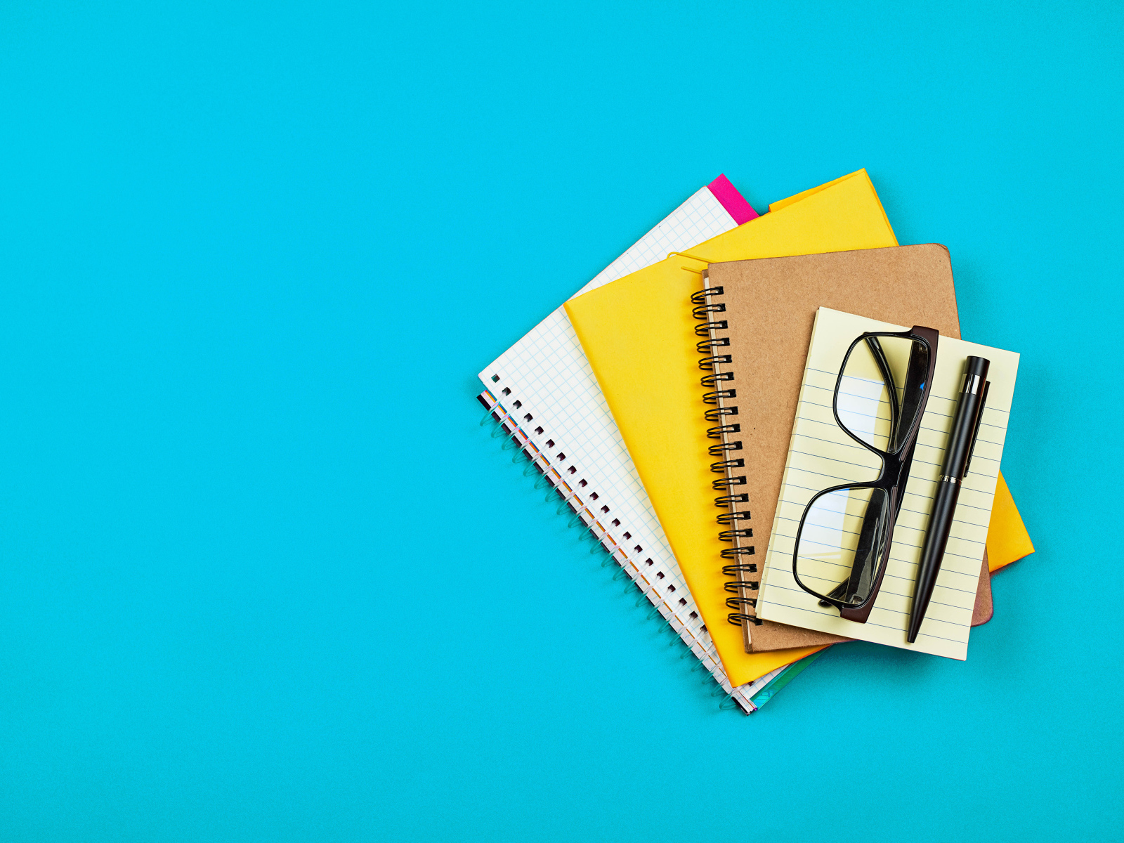 Блокноты, очки и ручка на голубом фоне