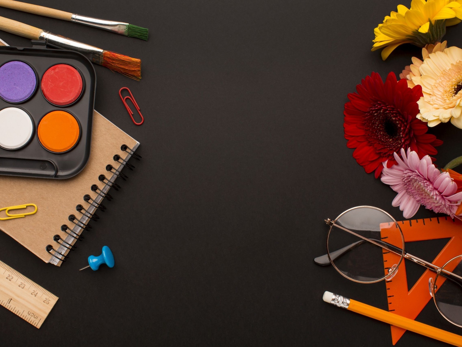 Канцелярские предметы, очки и герберы на черном фоне 