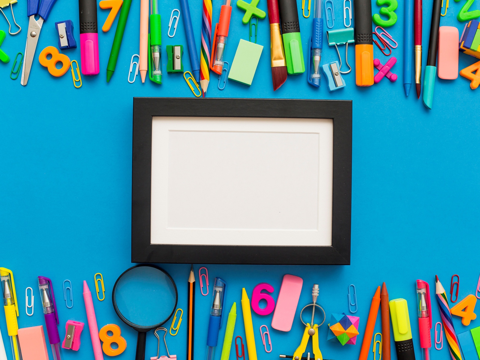 Белая рамка с разноцветными канцелярскими предметами на голубом фоне