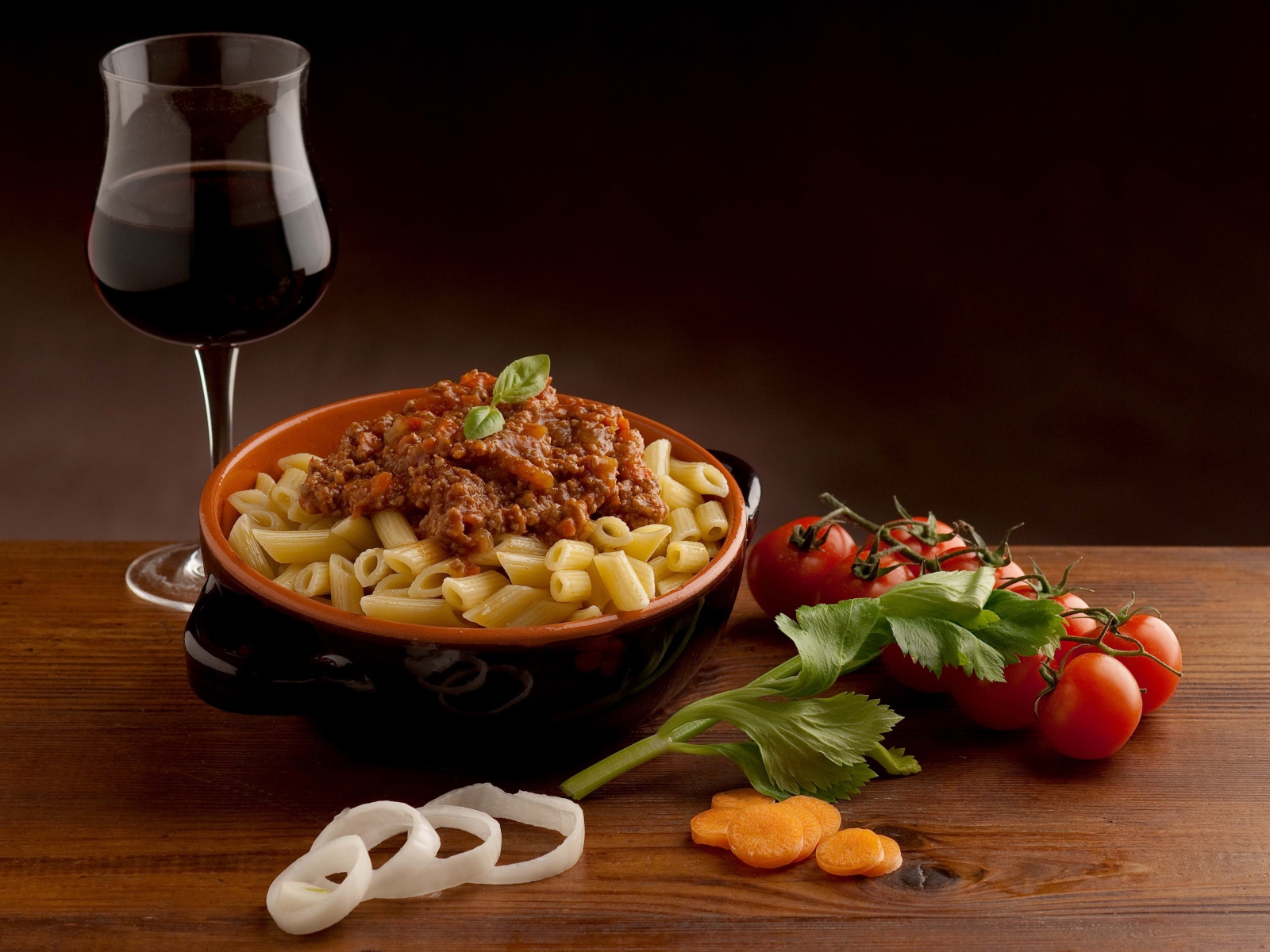 Макароны с фаршем на столе с бокалом вина и помидорами