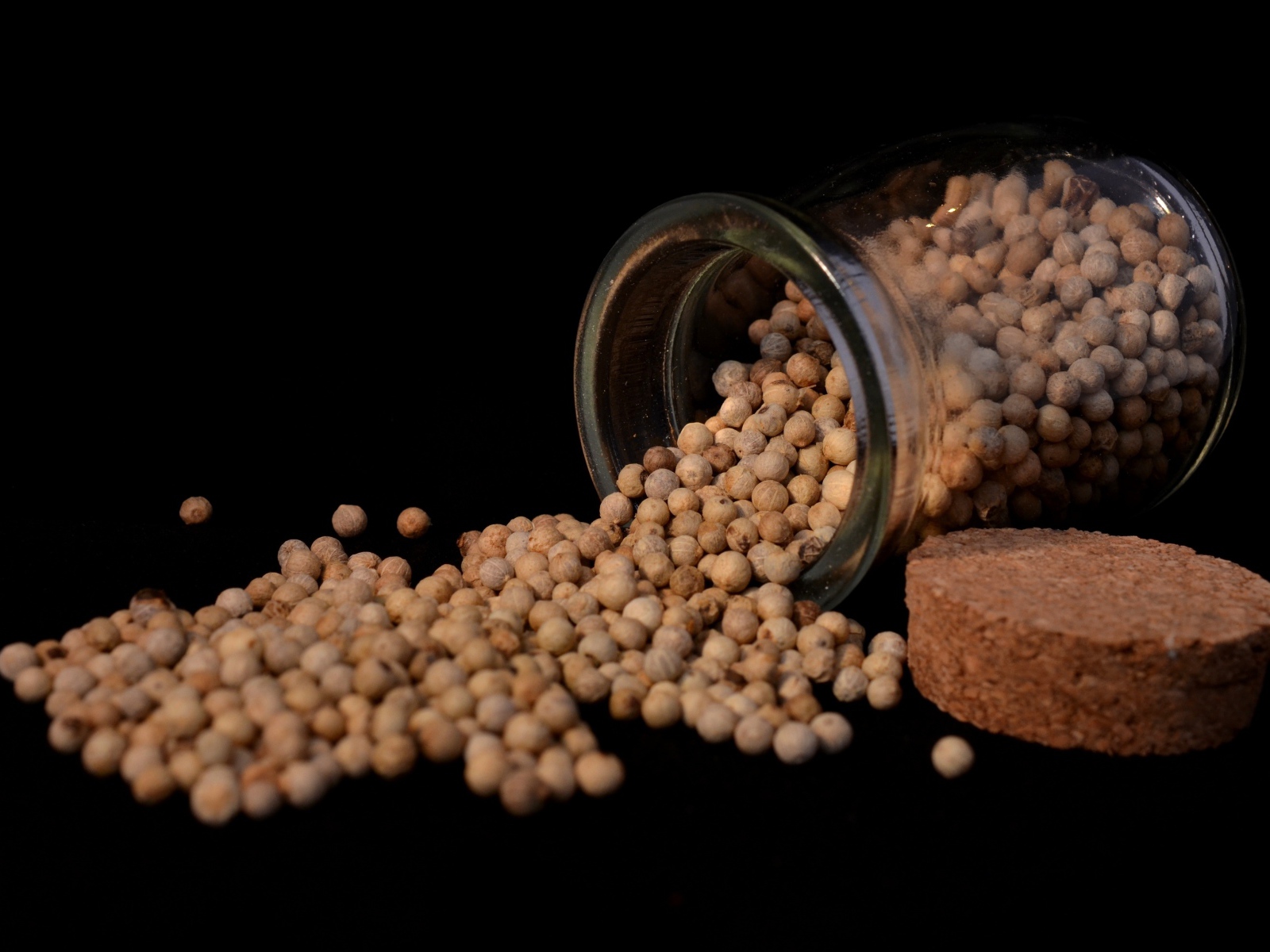 Перец горошек в стеклянной банке на черном фоне 