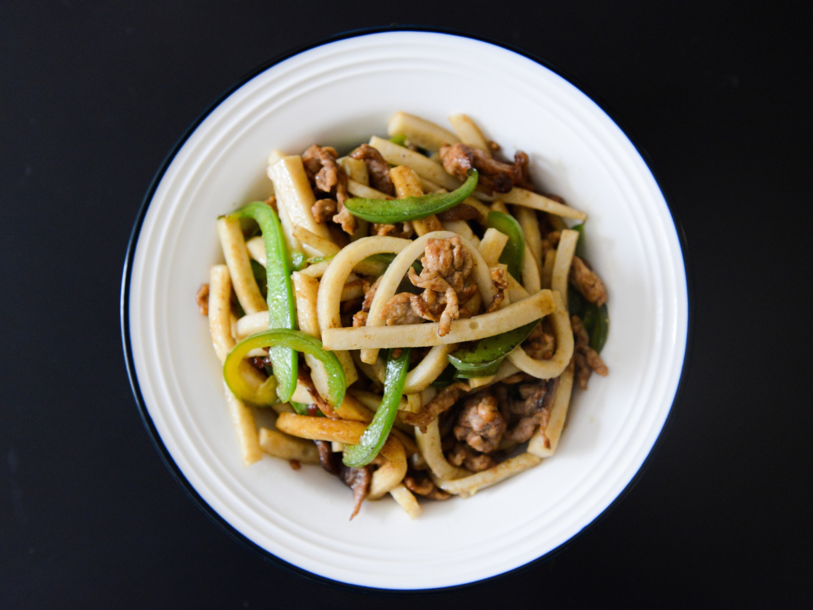 Салат с мясом в белой тарелке на черном фоне