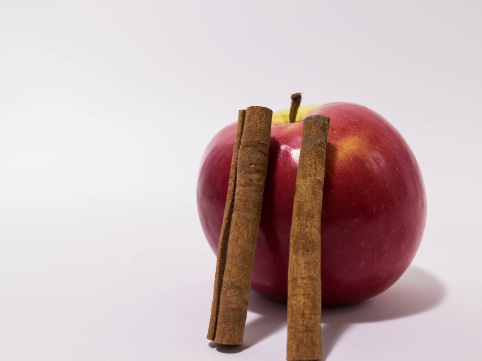Красное яблоко с палочками корицы на сером фоне