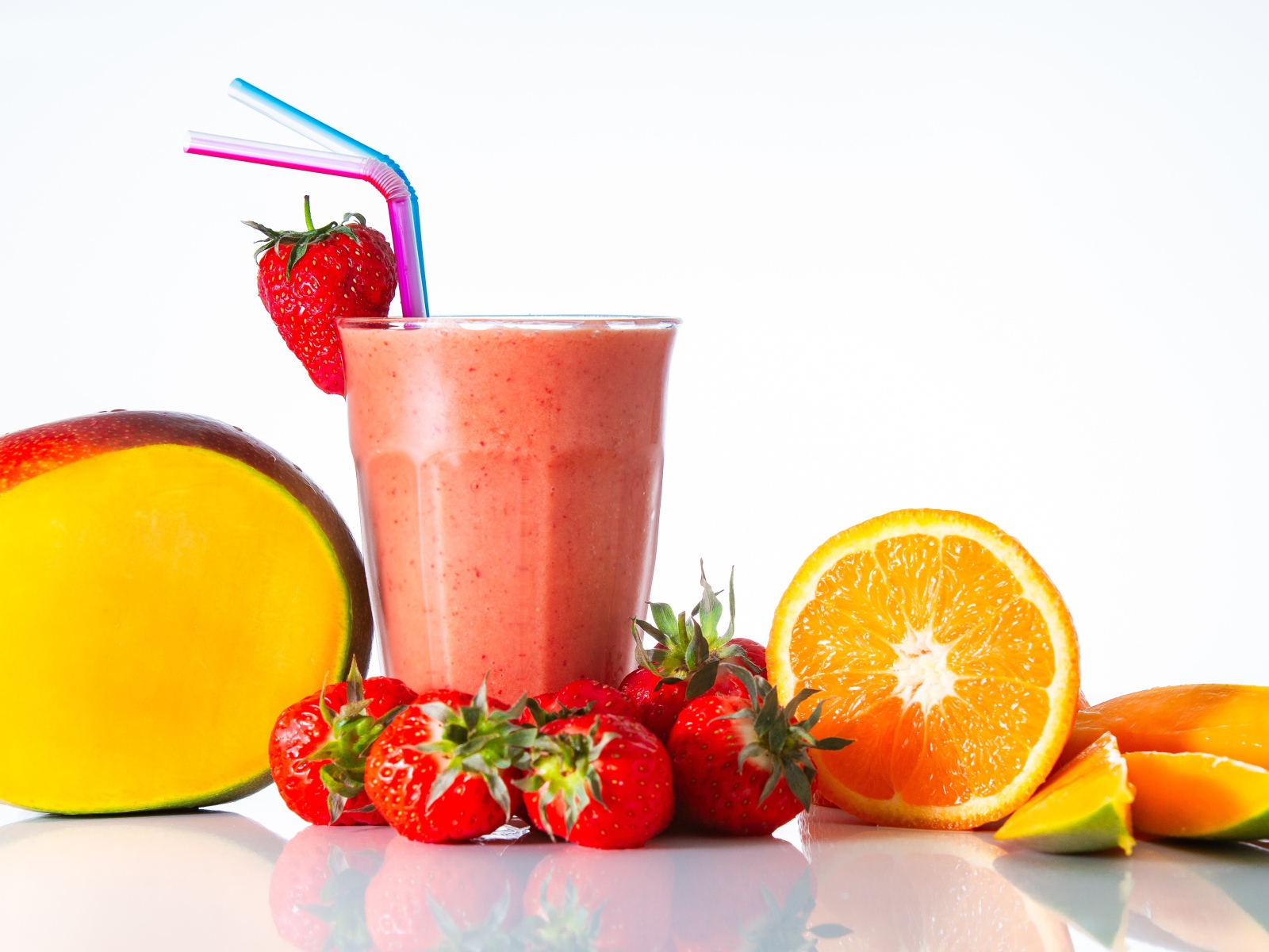 Спелое манго с клубникой и апельсином на столе со смузи