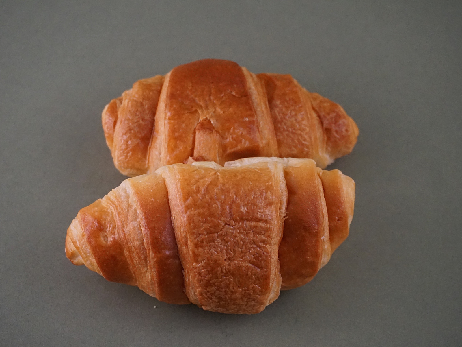 Two fresh croissants on a gray surface