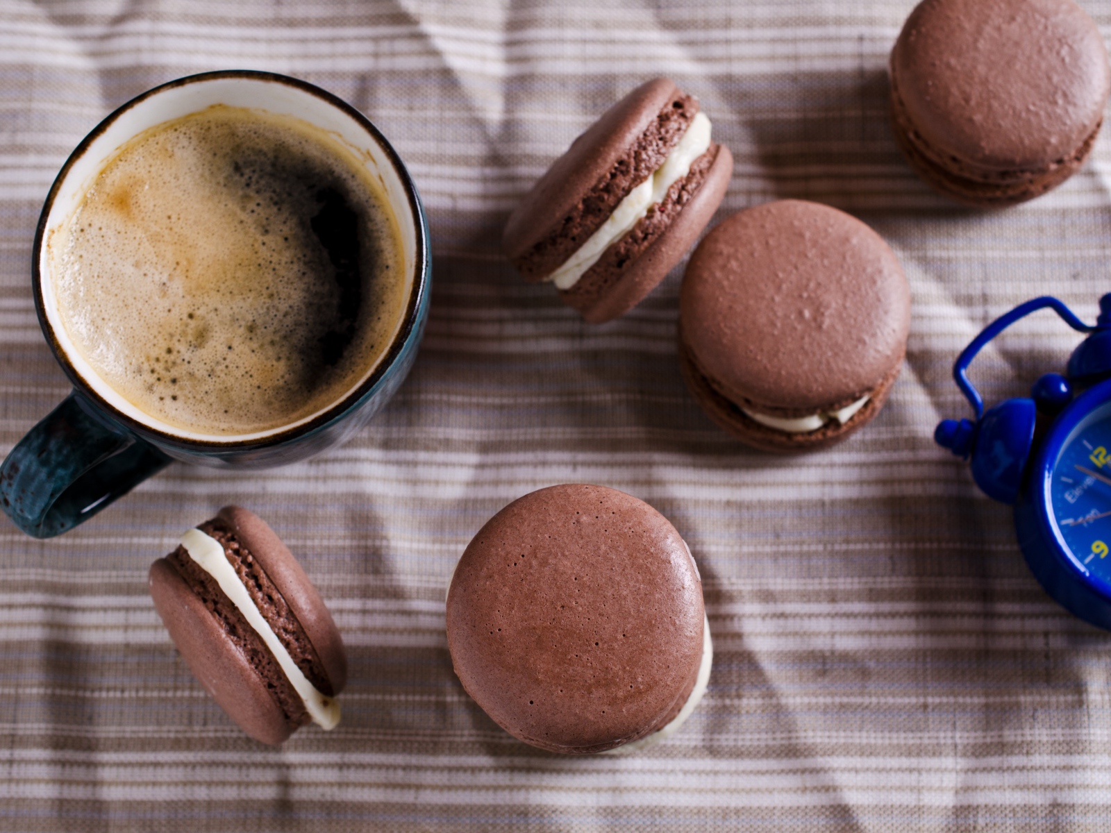 Чашка кофе на столе с десертом макарун и будильником