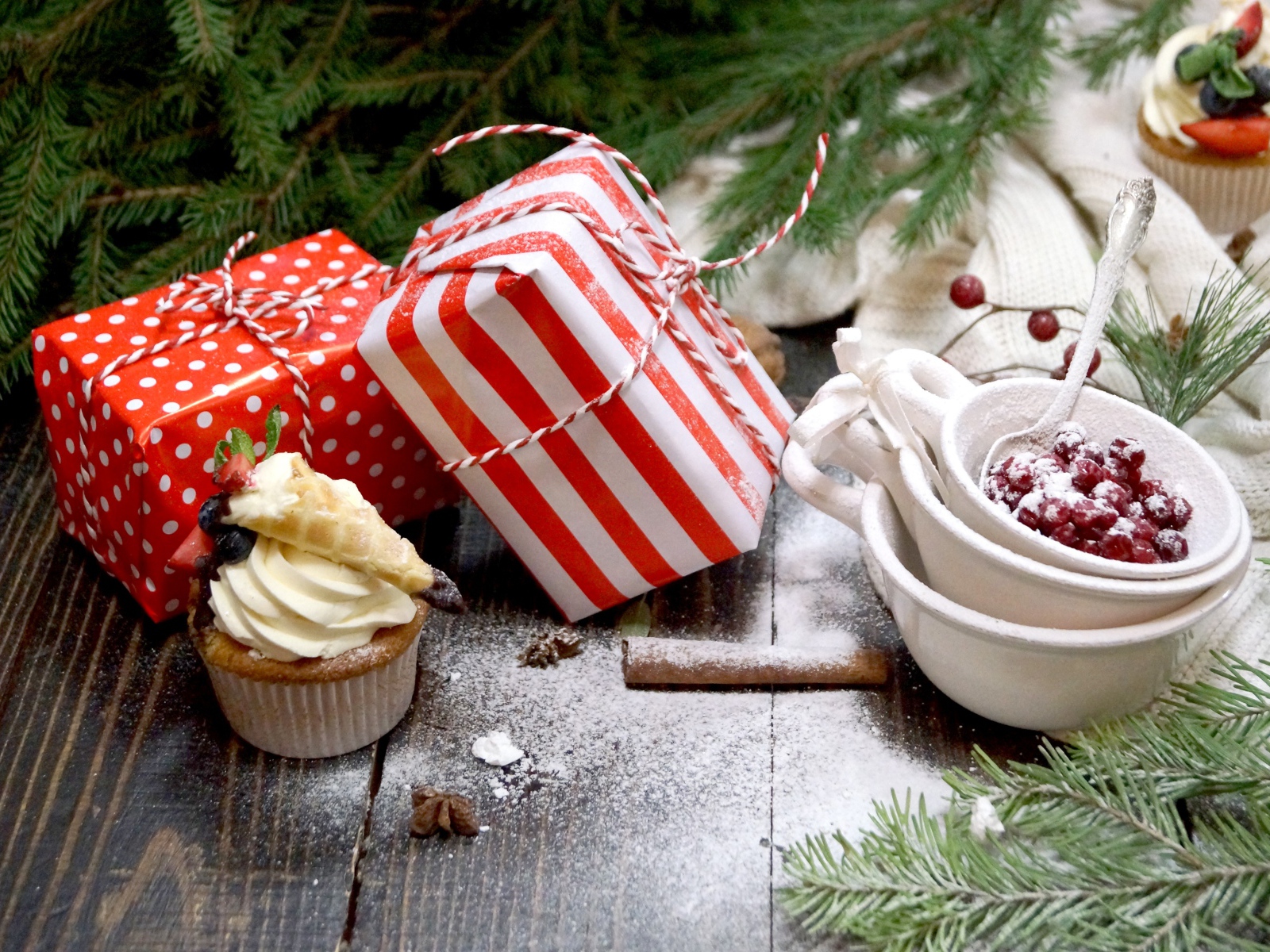 Два подарка на столе с еловой веткой и кексами 